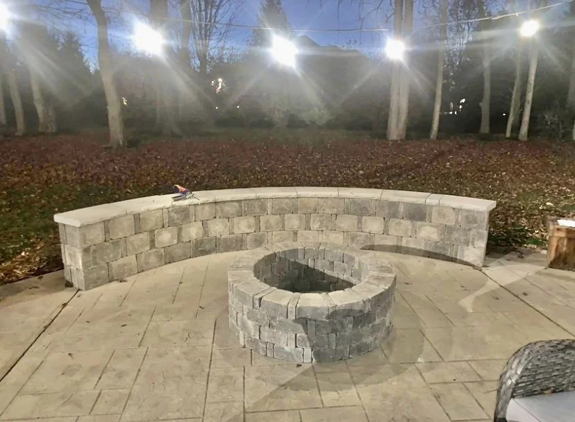 Stone firepit and curved seating wall on a stamped concrete patio at dusk